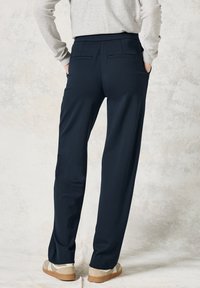 Pantalon bleu marine à coupe droite, en tissu lisse, avec deux poches arrière et une taille élastique, assorti à des chaussures légères.