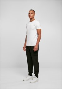 Witte T-shirt met korte mouwen, zwarte cargobroek met zakken en witte sneakers. Model staat rechtop met het gezicht naar voren tegen een neutrale achtergrond.