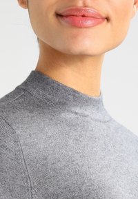 Pull à col roulé gris confectionné dans un matériau tricoté doux, avec un design ajusté et des bords sans couture pour une finition lisse.