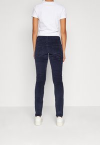 Mörkblå kordflosbyxor med slim fit, som har två bakfickor och en medelhög midja. Kombineras med en enkel vit t-shirt och vita sneakers.