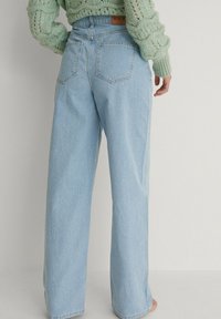 Ljusblå vida jeans i denim, med två bakfickor och en sydd midja med en logotyp. Texturen verkar jämn.