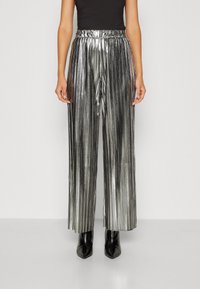 Metalické stříbrné plisované kalhoty s širokými nohavicemi a elastickým pasem, které jsou doplněny černými botami na podpatku s špičatou špičkou, vytvářejí elegantní vzhled.