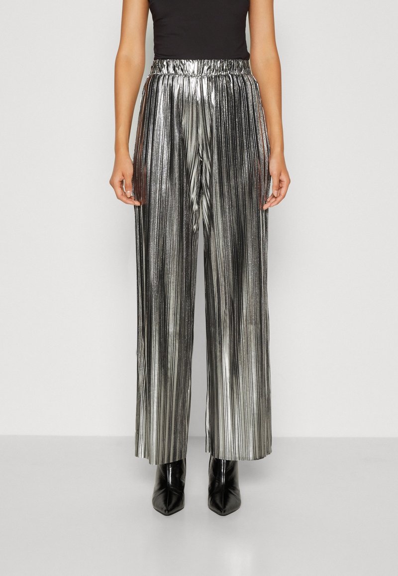 Metalické stříbrné plisované kalhoty s širokými nohavicemi a elastickým pasem, které jsou doplněny černými botami na podpatku s špičatou špičkou, vytvářejí elegantní vzhled.