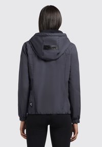 Veste courte gris foncé avec capuche, poignets et taille élastiques. Présente un patch logo au dos et une texture lisse et brillante.