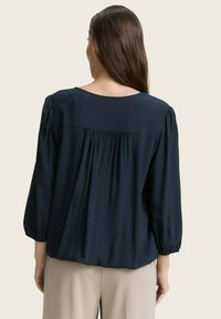 Marineblaue Bluse mit plissiertem R�ücken, Rundhalsausschnitt und langen, gerafften Ärmeln. Hergestellt aus einem glatten, leichten Stoff.