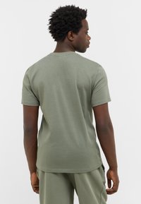 Oliwkowa koszulka z krótkim rękawem, okrągłym dekoltem i gładką, bawełnianą fakturą. Posiada dopasowany krój i proste wykończenie dołu.