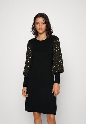 Robe noire avec un col rond, corps ajusté et manches bouffantes présentant un motif à pois dorés sur un tissu noir. Texture lisse dans l'ensemble.