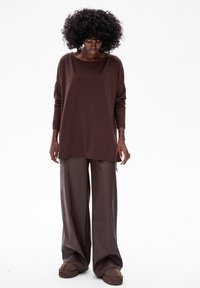Bruine langemouwen top met een ruime halslijn, gecombineerd met loszittende bruine satijnen broeken, beide met zachte texturen en een ontspannen silhouet.