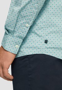 Lichtblauw overhemd met lange mouwen met een geometrisch patroon in rood en donkerblauw. Bevat knopen op de manchetten en een label op de onderste zoom.