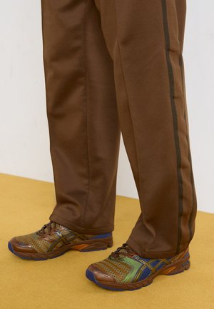 Pantalons de sport marron avec des bandes latérales associés à des chaussures de course colorées et texturées en matériaux en maille et synthétiques.