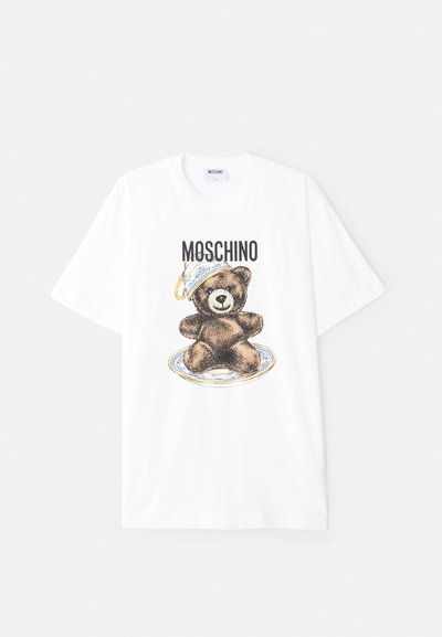 Valge puuvillane T-särk, millel on prinditud kujutis pruuni karu plaadil, kelles on sinine ja kuldne kauss. "Moschino" tekst kujutise kohal.