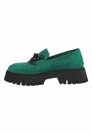 Mocassin en daim vert avec une semelle en caoutchouc noire épaisse, agrémenté d'une chaîne décorative noire sur l'avant. Texture lisse et design à enfiler.
