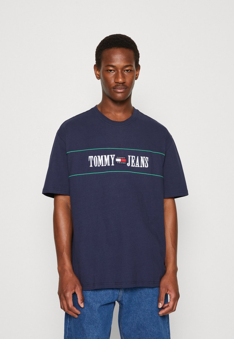 T-shirt di cotone blu navy con un logo bianco "TOMMY JEANS" in evidenza e strisce verdi, vestibilità rilassata, design a girocollo, maniche corte.