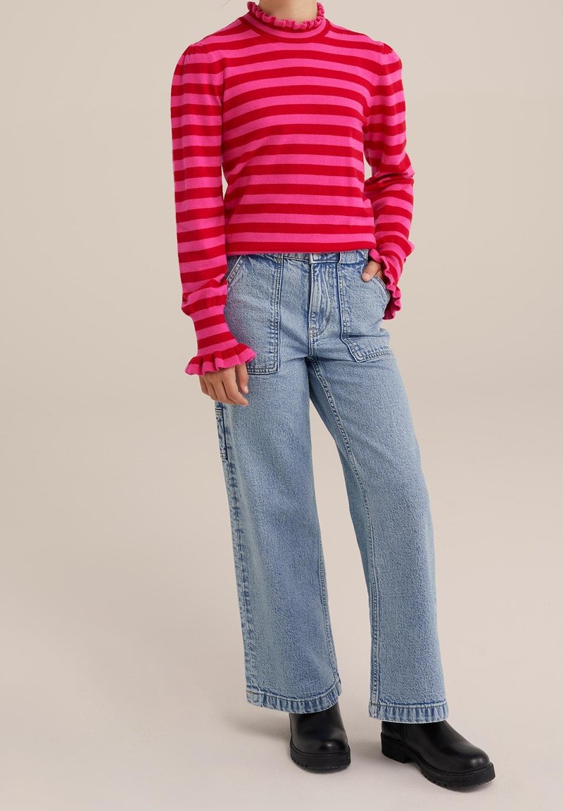 Personne portant un haut à manches longues rayé rouge et rose avec des poignets volantés, un jean taille haute bleu clair et des bottines noires.
