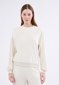 Felpa leggera color crema con scollo rotondo, maniche lunghe a raglan e polsini e orlo ribattuti. Texture liscia e vestibilità comoda.