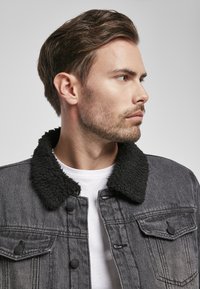 Tumši pelēkas džinsa jaka ar melnu pūkainu apkakli. Iekļauj pogas ar spiedpogām un divas krūšu kabatas. Valkāta virs vienkārša baltā T-kreklu.