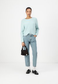 Lys blå strikket genser, høy midje lys denimjeans, svart håndveske, og svarte mokasiner med hvite sokker. Enkelt, teksturert design.
