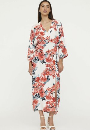 Maxi jurk met bloemenprint, voorzien van een witte achtergrond met rode en blauwe bloemen, V-hals, lange mouwen en een zijsplit. Lichtgewicht stof.
