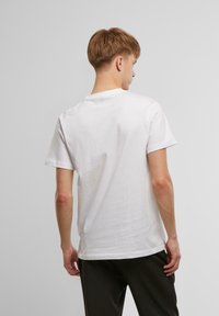 White cotton t-shirt with short sleeves, crew neckline, and a relaxed fit, viewed from the back, featuring a smooth texture.