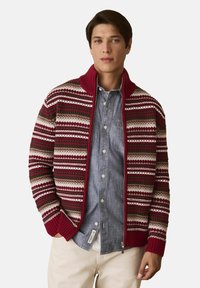 Knit cardigan with a maroon base, featuring horizontal stripes in beige, green, and red. Ribbed cuffs and collar; front zipper closure.