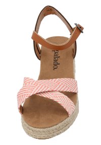 Sandalia tipo espadrille con una cinta de lona en un patrón de zigzag en blanco y naranja claro. Presenta una correa en el tobillo de color marrón y una suela de plataforma de yute trenzado.