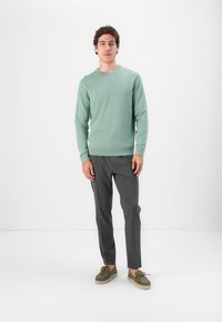 Jasnozielony sweter z okrągłym dekoltem, szare dopasowane spodnie i zielone buty typu slip-on z brązowymi sznurówkami. Gładka, teksturowana tkanina. Minimalistyczny design.