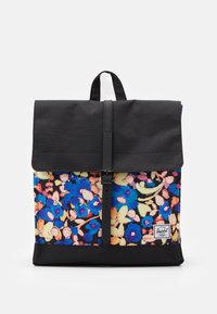 Sac à dos en tissu noir avec un motif floral en bleu, rose et jaune. Il est doté d'une fermeture à rabat avec une boucle noire. Possède un patch logo blanc.