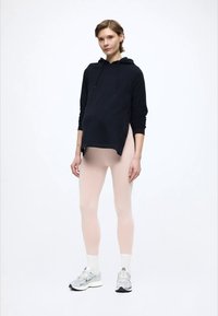 Fekete kapucnis pulóver húzózsinórokkal, világos rózsaszín leggingsszel és szürke sportcipőkkel kombinálva. A szett lazított szabású és puha anyagú.