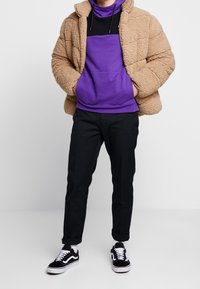 Tan fluffig lammskinnsjacka, lila och svart hets hoodie, svarta smala byxor och svarta Vans sneakers med vita accenter.