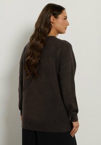 Maglione marrone, sovradimensionato, realizzato in tessuto morbido. Presenta maniche lunghe, polsini a coste e un orlo arrotondato con dettagli minimi.
