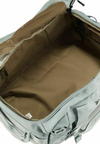 Bolsa de viaje azul claro con un interior amplio y vacío. Cuenta con un forro beige, un bolsillo de malla y cremalleras y correas resistentes. Textura suave.