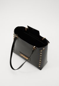 Borsa a mano in pelle nera con dettagli in metallo dorato, borchie e manico superiore. Presenta una placca con logo e un interno aperto che mostra una finitura testurizzata.