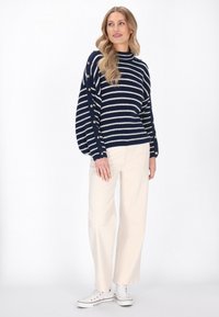 Gestreifter Pullover in Marineblau und Weiß mit Ballonärmeln, ausgestattet mit Knopfdetails an den Ärmeln. Kombiniert mit cremefarbenen, weiten Hosen und weißen Sneakern.