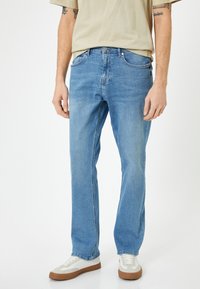 Jeans de mezclilla azul claro con un diseño de pierna recta, un ligero desvanecimiento, estilo de cinco bolsillos y detalles de costura visibles. Combinados con zapatillas blancas.