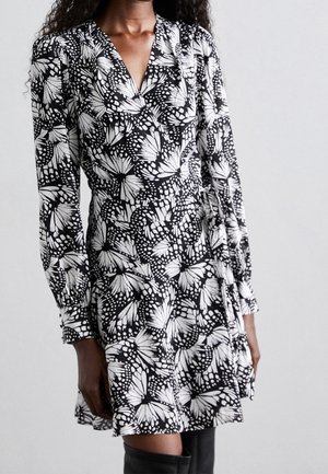 Zwart-witte wikkeljurk met een vlinderpatroon, lange mouwen en een getailleerde taille, gemaakt van lichtgewicht stof met een gladde textuur.