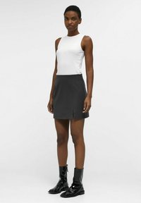 Un haut sans manches blanc associé à une mini-jupe noire avec une fente sur le côté. Des bottes de cheville noires et brillantes complètent la tenue.