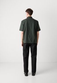 Korte mouw, donkergroen gestreept shirt met een kraag, gecombineerd met zwarte rechtlopende broeken en zwarte leren schoenen.