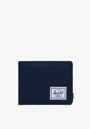 Cartera de tela en color marino con textura suave, que presenta una etiqueta blanca con texto en color marino y un pequeño acento de rayas rojas y blancas en el lateral.