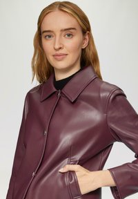 Burgunderfarbene Lederjacke mit spitzem Kragen, zwei Fronttaschen und Knopfverschluss. Glatte Textur, elegantes Design und taillierte Silhouette.