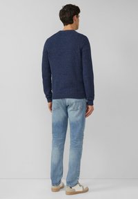 Granatowy teksturowany sweter z dzianiny z okrągłym dekoltem, noszony z jasnoniebieskimi dżinsami i codziennymi trampkami, widziany od tyłu.