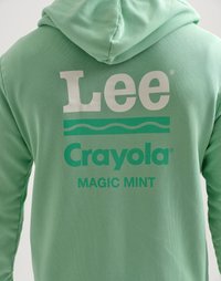 Persona che indossa un hoodie verde menta con la scritta "Lee," "Crayola," e "MAGIC MINT" stampata sul retro in testo bianco e verde.