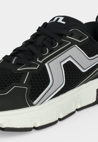 Chaussure de sport noire avec tige en mesh, détail zigzag réfléchissant gris, lacets noirs et semelle blanche épaisse texturée.