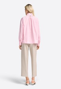 Blusa a righe rosa con colletto alto e schiena arricciata, abbinata a pantaloni larghi beige e sandali con tacco neutri.