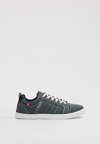 Zapatilla de lona gris con suela de goma blanca, punta redonda y acentos en navy contrastantes. Presenta costuras decorativas y el logo de la marca en el costado.