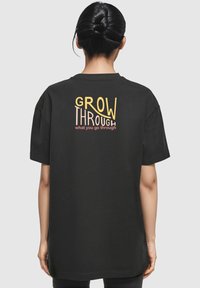 Sort t-shirt med korte ærmer, der har teksten "GROW THROUGH what you go through" trykt i gul og pink på bagsiden.