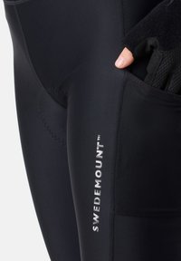 Schwarze, eng anliegende Radsporttight mit strukturiertem Einsatz, sichtbaren Nähten und reflektierendem "SWEDEMOUNT"-Logo an der Seite.