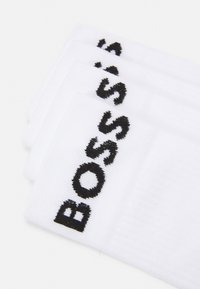 Valged puuvillased sokid, millel on musttikkimisega "BOSS" logo. Sile tekstuur ja soonikkoeline disain äärekraes. Kolme paari pakis.