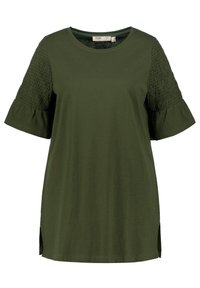 Olivgrön T-shirt med smockat stickningsdetaljer på ärmarna och urtagna korta ärmar. Har sidospalter vid fållen för ökad komfort.