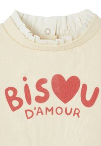 Cremfarbendes Kleidungsstück mit einem Rüschenausschnitt, verziert mit rotem Druckschriftzug "BISOU D'AMOUR" und einem Herzsymbol. Geschmeidige Textur und lässiges Design.
