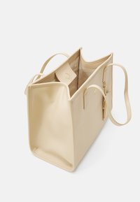 Beige synthetische draagtas met een gladde textuur, open bovenkant, dubbele handvatten, een binnenzak en een ritssluitingsdetail aan de zijkant.